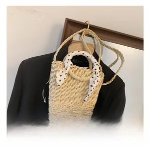 Detail view of beige woven straw bucket bag with red silk scarf handle and long shoulder strap