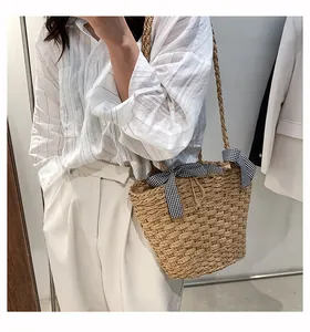 Dettaglio borsa tote in paglia intrecciata a mano con fiocchi a quadretti neri e tracolla lunga