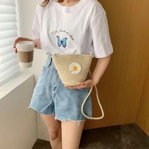 Détail du sac seau en paille tissé à la main avec fleur de marguerite blanche en tricot