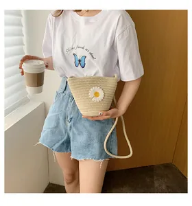 Détail du sac seau en paille tressée beige avec marguerite blanche et bandoulière