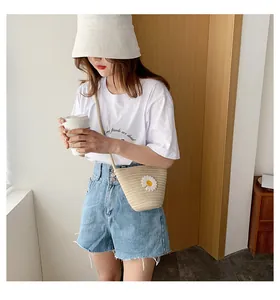 Détail d'un sac seau en paille beige avec fleur de marguerite 3D et fine bandoulière