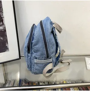 Detail van een denim mini-rugzak met dubbele zwarte ritsen en een handig zijvakje