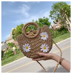 Detail of straw bag featuring white daisy decor and woven circular handles in outdoor light