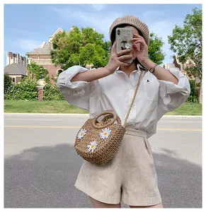 Outdoor shot of a woven straw basket bag with white daisy embroidery and drawstring liner