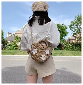Detail of straw crossbody bag featuring white daisy patches and a drawstring liner