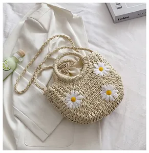 Detail of straw woven bag with white daisy flowers and round ring handles on white bedding
