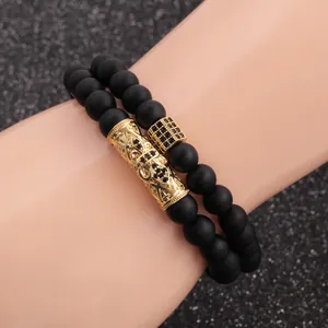 Detail of matte black beaded bracelets with gold hollow metal charms on hand model