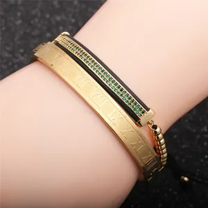Nahaufnahme von Goldarmreif mit römischen Ziffern und schwarzem Armband mit grünem Zirkon