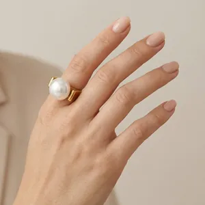 Detailansicht eines goldenen geometrischen Rings mit einer großen weißen Perle am Modellfinger