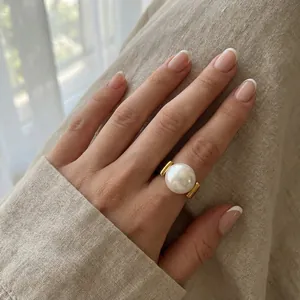 Detailansicht eines eleganten großen weißen Perlenrings mit Goldakzenten an der Hand