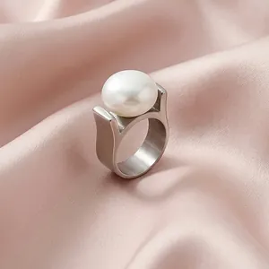 Makro-Detail eines silbernen Edelstahlrings mit großer weißer Perle auf rosa Seidenstoff