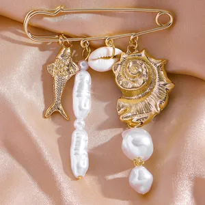 Détail d'une broche épingle dorée avec des breloques coquillages et des perles baroques.
