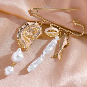 Détail d'une broche dorée ornée de breloques en coquillage, poisson et perles baroques