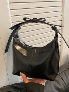 Glossy black patent leather crescent bag with bow detail held by a model
