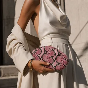 Close-up detail of an irregular pink snake print acrylic evening clutch held by a model.