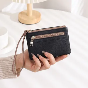 Handheld black pebble leather wallet featuring dual gold zippers and a wristlet strap