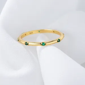 Macro detail of gold-plated S925 silver ring with small green zircons on white fabric