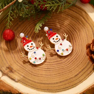 Close-up of enamel snowman earrings with red hat and pearl on a rustic wooden background
