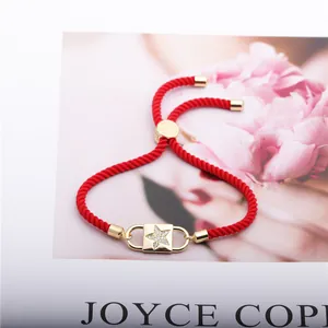 Detail of red braided cord bracelet with a gold star pendant and sparkling zircons