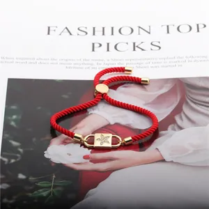 Detail of red braided rope bracelet with a gold star-engraved zircon padlock charm