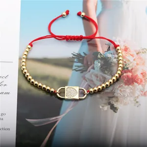 Macro detail of hand-woven red cord bracelet with gold lock charm and inlaid crystals