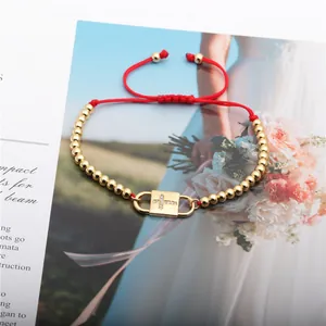 Detail of red braided cord bracelet with gold beads and sparkling zircon cross lock charm
