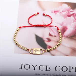 Detail of red woven bracelet with a gold-tone cross charm and adjustable pull cord