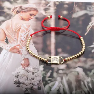 Detail of red braided bracelet with gold beads and zircon crescent moon lock pendant
