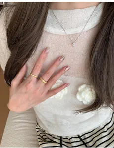 Detail of woven wheat pattern gold rings and a delicate silver pendant necklace on a model