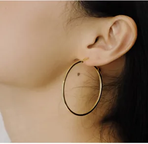 Close-up of model wearing large minimalist gold-plated hoop earrings with a mirror finish