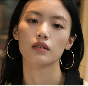 Close-up of model wearing large rose gold hoop earrings with minimalist metal finish