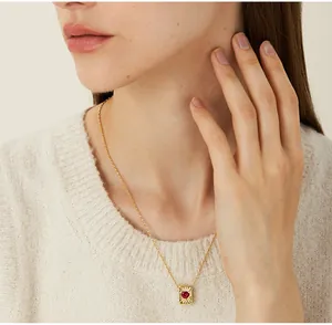 Detailopname van een gouden vierkante hanger met hartrobijn op een dames sweater