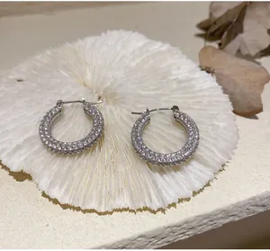 Detailed view of silver hoop earrings featuring pavé-set crystals on white textured stand