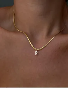 Primer plano de un collar de cadena de serpiente dorada con un colgante de letra R brillante