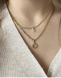 Primer plano de cadena de serpiente dorada con colgante S y collar de carita con diamantes