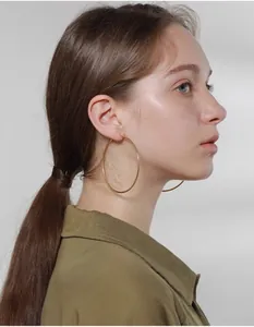 Close-up of model wearing large polished gold hoop earrings in minimalist titanium steel