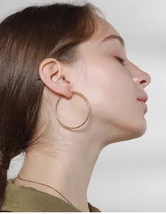 Close-up of a model wearing large minimalist golden hoop earrings in polished steel