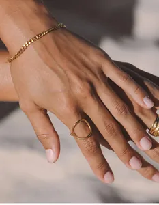 Detail of a woman wearing gold-toned oval rings and a curb chain bracelet for daily styling