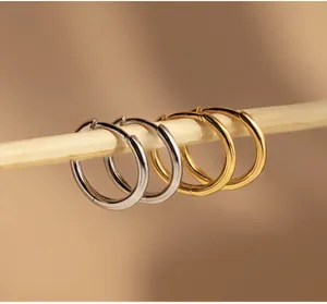 Polished gold and silver hoop earrings hanging on a natural wood bar in a close-up detail