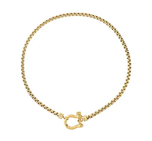Détail d'un collier chaîne à mailles carrées dorées avec fermoir fer à cheval chic