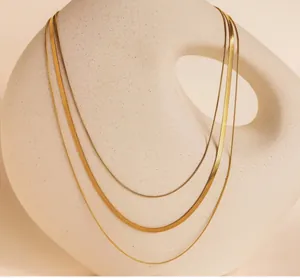 Detail view of a triple-layered golden snake chain necklace set on a ceramic stand