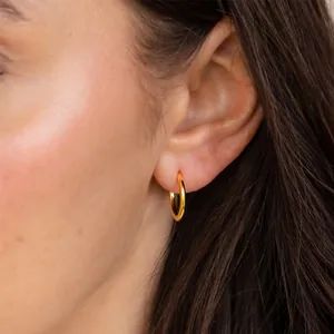 Minimalist gold hoop earrings worn on ear showing high-shine metallic texture