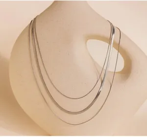 Close-up of triple-layered silver snake chain necklace on a ceramic art vase