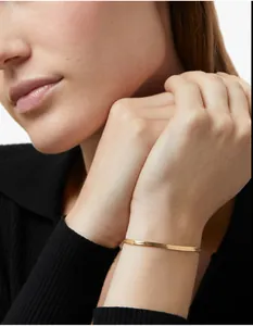 Detailed view of a gold flat snake chain bracelet on a model wrist for luxury styling