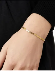 Close-up of a sleek gold flat snake chain bracelet on a wrist with black knit background