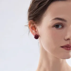 Orecchini a perno tondi rosso scuro lucidi su una modella, con perni in argento S925