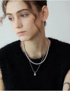 Close-up of a double-layered silver necklace with bead chain and teardrop pendant
