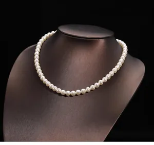 Gros plan d'un collier de perles blanches lustrées sur un buste métallique sombre