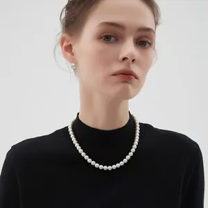 Élégant collier de perles blanches rondes et boucles d'oreilles sur un pull noir