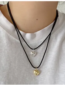 Nahaufnahme minimalistischer Herzanhänger in Gold und Silber an schwarzen Kordeln